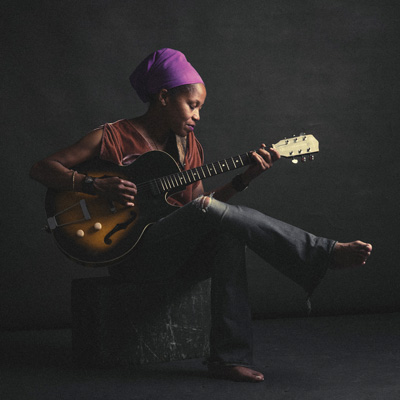 J.R. Fhodes, seated, playing a hollow-bodied electric guitar