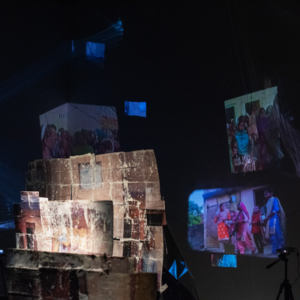 Structures made of collaged prints in a dimly lit space with a number of projected images of various sizes on the wall behind them.