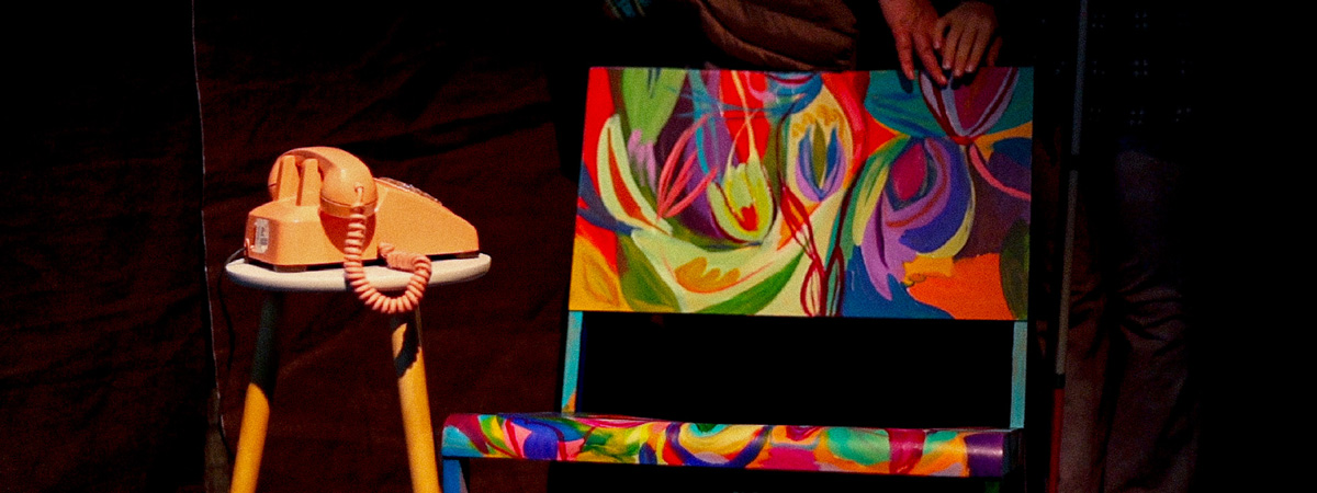 A colorfully-painted chair next to a stool with a corded telephone on it.
