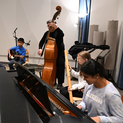 Michael Bisio plays upright bass while three students play guitar, piano, and rain stick.