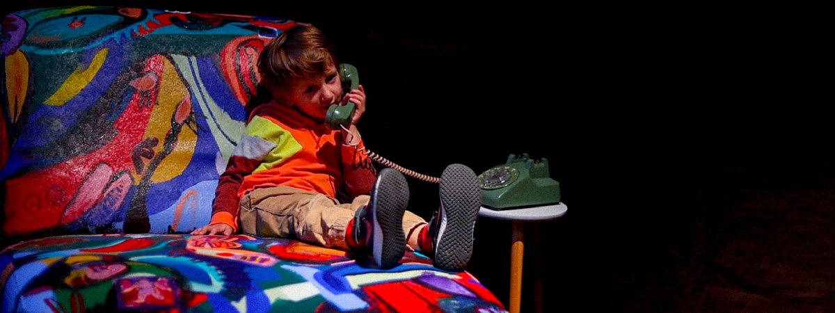 A child seated on a colorfully painted couch, holding a rotary phone receiver to his ear.