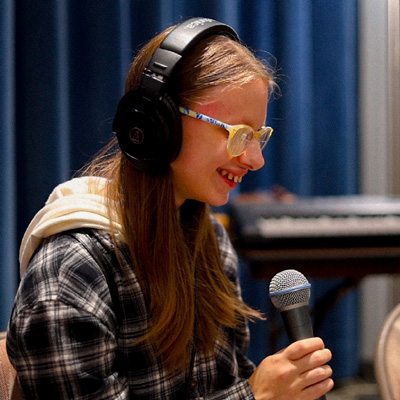 A student holding a microphone and wearing headphones, smiling.