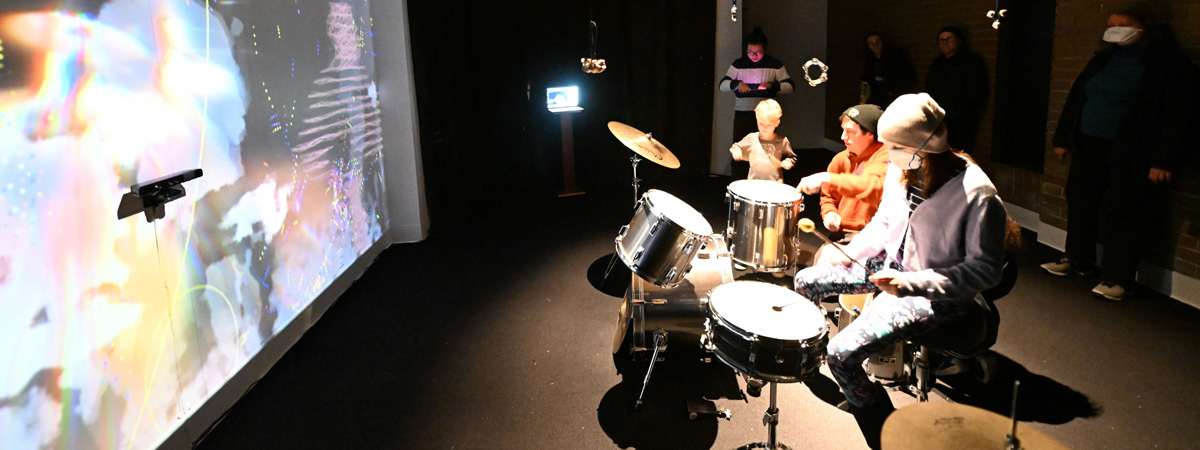 People sitting at and around a drum kit in a darkened room with