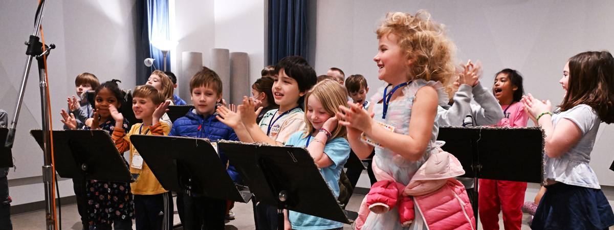A group of children in a recording studio, clapping.