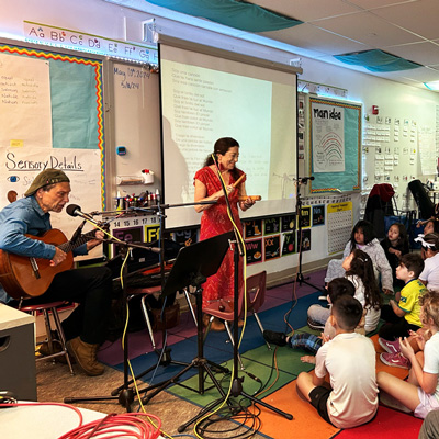 Abel Rocha and Madeleine Sosin playing guiar and clave with a classroom of children.