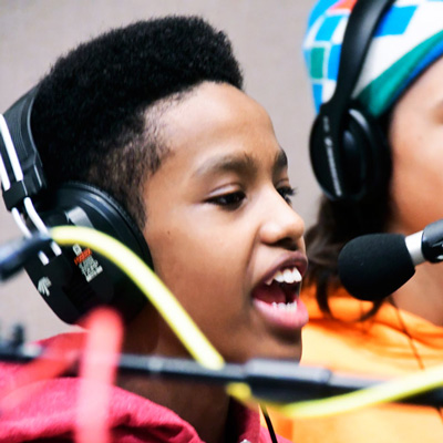 A boy wearing headphones, speaking into a microphone.