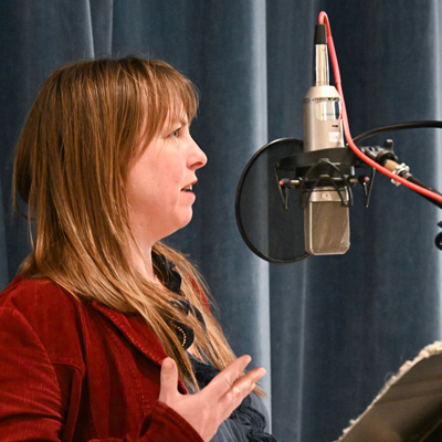 Becca Rose Hall, in profile, speaking into a microphone.