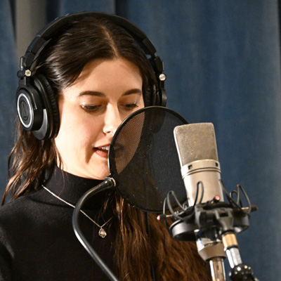 Elyse Hauser, wearing headphones, speaking into a microphone.