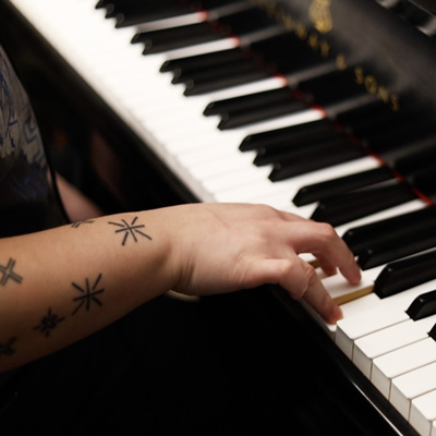 A tattooed forearm and hand playing a piano keyboard.