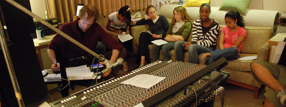 Several people seated in a room with a large sound mixing board in front of them.