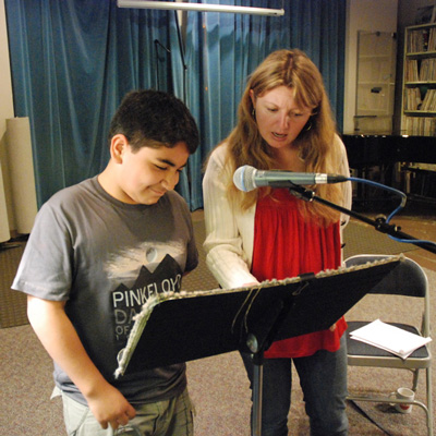 Two people standing looking down at a music stand with a a microphone in front of them.