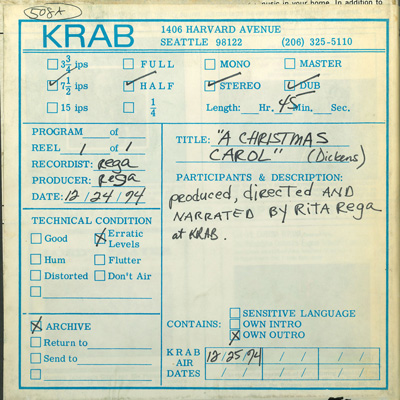 A reel-to-reel tape box from KRAB FM reading "A Christmas Carol (Dickens), produced, directed, and narrated by Rita Rega at KRAB," with a broadcast date of 12/25/74.